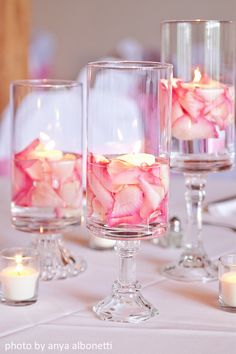 candles and flowers in glass vases on a white table cloth with pink roses inside