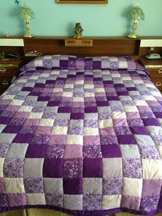 the bed is made with purple and white quilts