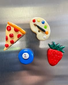 three magnets with different designs on them and one has a piece of pizza, the other is a strawberry