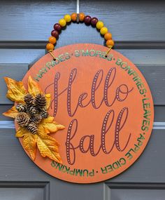 a sign that says hello fall hanging on a door with autumn leaves and pine cones