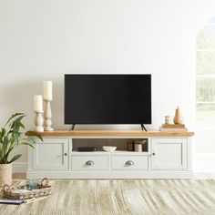 a flat screen tv sitting on top of a white entertainment center next to a potted plant