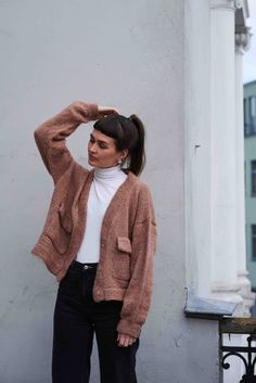 a woman standing in front of a building wearing a brown cardigan sweater and black jeans