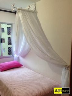 a bed with a white canopy and pink pillow on top of it in front of a window