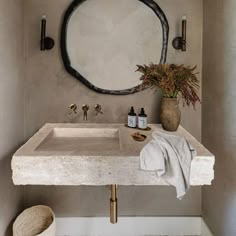 a bathroom sink sitting under a round mirror next to a vase with flowers on it