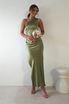 a woman in a green dress standing next to a white vase with flowers on it