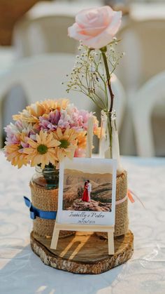 an arrangement of flowers in a vase on top of a wooden stand at a wedding reception