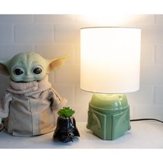 a baby yoda lamp sitting next to a small black object on a white table