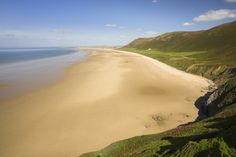 an aerial view of a sandy beach with green grass on the shore and hills in the background