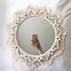 a hand holding a cell phone in front of a round mirror with fringes on it