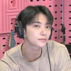 a young man wearing headphones sitting in front of a pink wall with guitars behind him