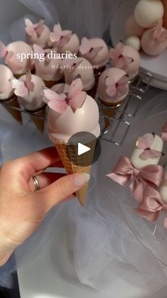 a person is holding an ice cream cone with pink bows on it and there are cupcakes in the background