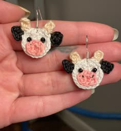 a hand holding two small crocheted cow earrings