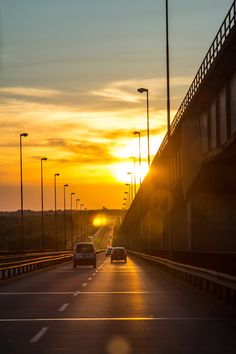 the sun is setting over an empty highway with cars driving down one side and street lights on the other