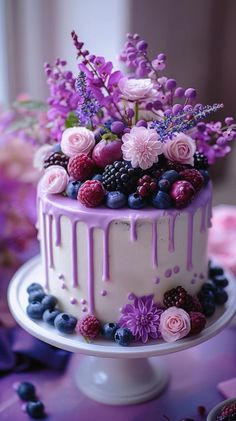 a white cake with purple icing and fresh berries on the top is surrounded by flowers