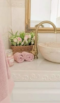 a white sink sitting under a bathroom mirror next to a basket filled with pink flowers