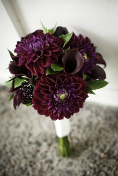 a bouquet of purple flowers sitting on top of a white vase next to a wall