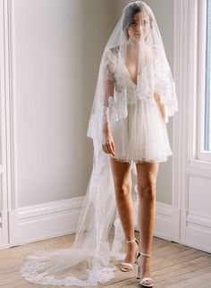 a woman in a white wedding dress and veil standing on a wooden floor with her legs crossed