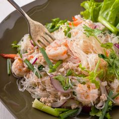 a salad with shrimp, carrots and lettuce on a plate next to a fork