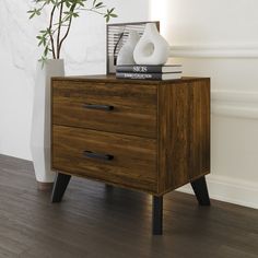 a wooden cabinet with two drawers and a vase on top, next to a plant