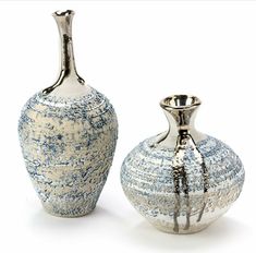 two silver vases sitting next to each other on a white surface with blue speckles