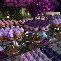 an assortment of desserts and sweets displayed on gold trays with purple flowers in the background