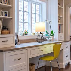 a kitchen with white cabinets, yellow chairs and a large window above the countertop