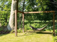 a hammock hanging from a wooden frame in the middle of a yard next to a tree