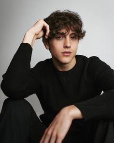 a young man sitting on the ground with his hands in his hair and wearing a black sweater