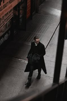 a man is walking down the street with a coat over his shoulders and a bag on his shoulder