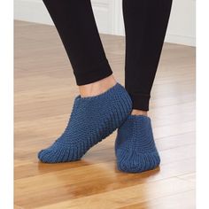 a woman's feet wearing blue knitted slippers on top of a wooden floor