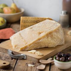 a block of cheese sitting on top of a wooden cutting board next to olives