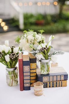 some books and flowers are sitting on a white tablecloth with two vases full of flowers