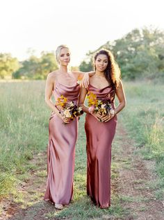 two beautiful women standing next to each other in front of a field with tall grass