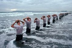 a group of men standing in the ocean with their hands on their head and looking at the water