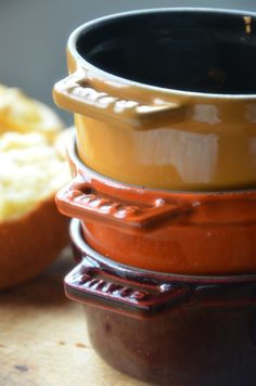 a stack of ceramic bowls sitting on top of a wooden table next to bread slices