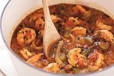 a white bowl filled with shrimp and vegetable soup on top of a table next to a wooden spoon