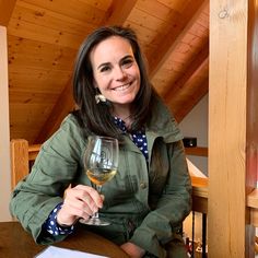 a woman sitting at a table with a glass of wine in her hand and smiling