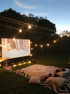 two people laying on a blanket in the grass watching a movie