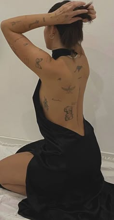 a woman with tattoos on her back sitting on a bed wearing a black dress and heels