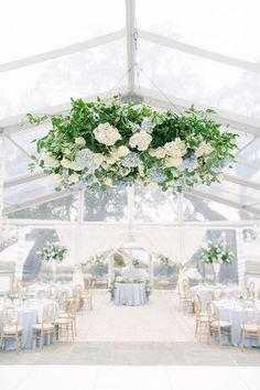 the inside of a tent with tables, chairs and flowers hanging from it's ceiling