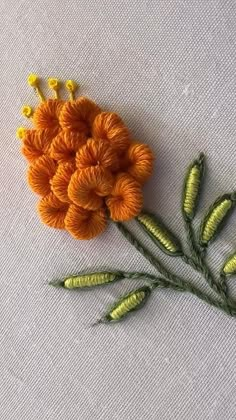 an orange flower with green stems on a white cloth background, and some yellow flowers in the middle