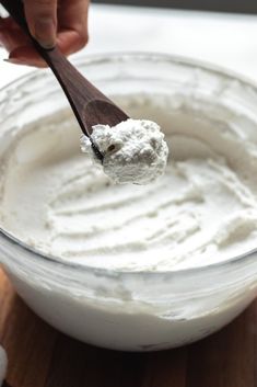 a person holding a wooden spoon over a bowl filled with white dip and sour cream