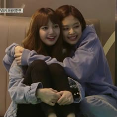 two young women sitting next to each other on top of a couch with their arms around each other