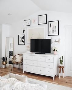 a living room with white furniture and framed pictures on the wall, including a flat screen tv