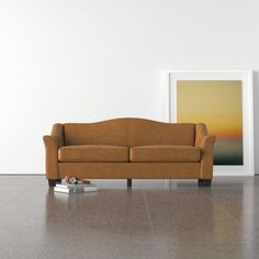 a couch sitting on top of a hard wood floor next to a framed painting and remote control