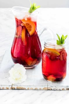 two pitchers filled with liquid sitting on top of a white marble counter next to a flower