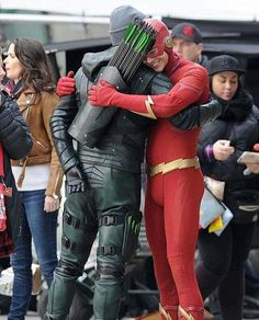 two people dressed as the flash and green arrow hugging each other in front of a crowd