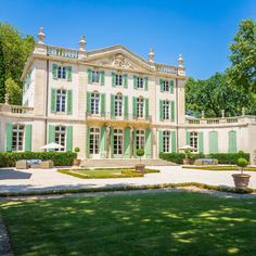 a large white house with green shutters on the front and side windows, surrounded by lush greenery