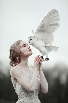 a woman holding a white bird in her hand and looking up at it's wings