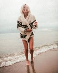 a woman is walking on the beach in her bathrobe and holding a drink